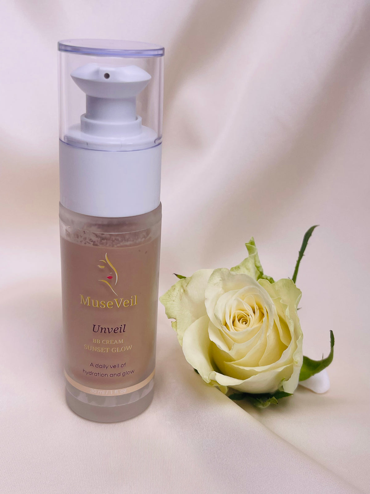 MuseVeil Unveil Hydration Mist in a clear pump bottle with a white cap, displayed next to a white rose on a draped cream fabric background.